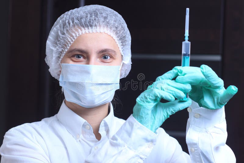 Medico femminile del ritratto nella maschera medica con l'iniezione della siringa immagine stock