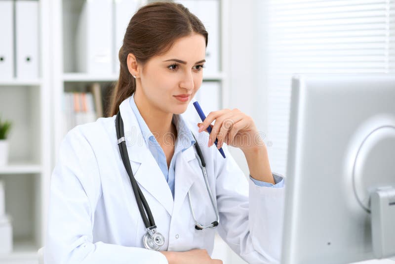 Medico femminile dell'America latina che si siede alla tavola e che lavora dal computer all'ufficio dell'ospedale Il medico o il fotografia stock libera da diritti Medico femminile dell'America latina che si siede alla tavola e che lavora dal computer all'ufficio dell'ospedale Il medico o il fotografia stock libera da diritti
