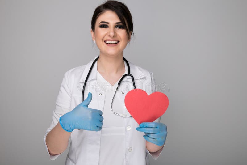 Medico femminile grazioso con lo stetoscopio e l'immagine del pollice di rappresentazione del cuore isolato sopra i precedenti gr immagini stock Medico femminile grazioso con lo stetoscopio e l'immagine del pollice di rappresentazione del cuore isolato sopra i precedenti gr immagini stock
