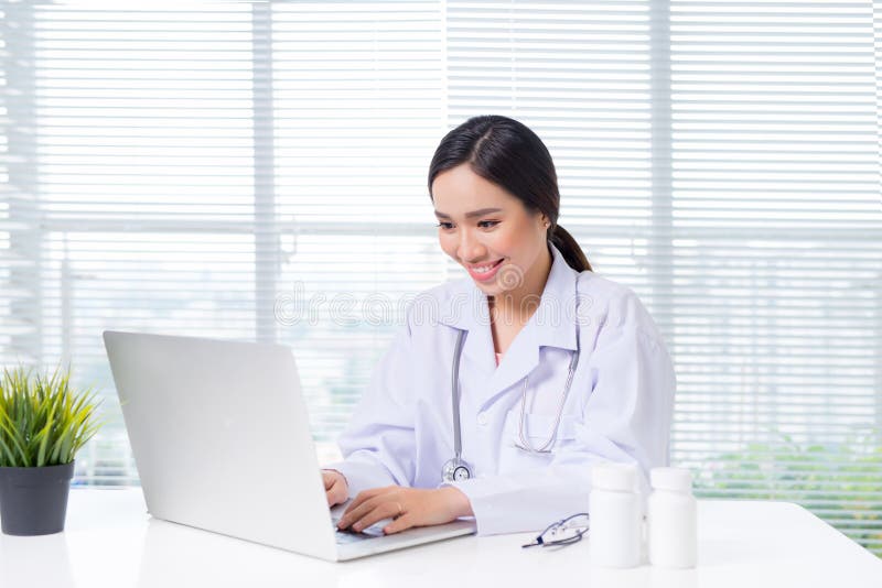 Medico femminile sorridente dei giovani che si siede alla scrivania ed a w di lavoro immagini stock libere da diritti Medico femminile sorridente dei giovani che si siede alla scrivania ed a w di lavoro immagini stock libere da diritti