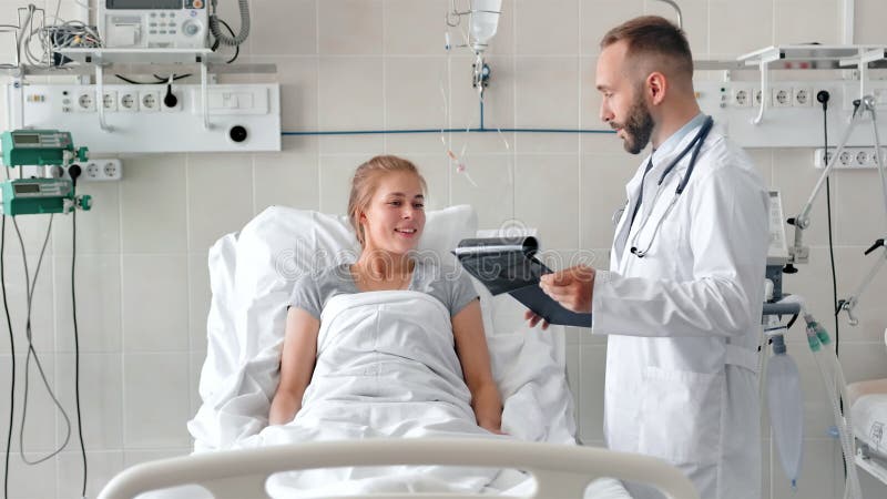 Medico maschio che parla con paziente femminile nel letto di ospedale Medico sorridente con la lavagna per appunti ed i raggi x r video d archivio Medico maschio che parla con paziente femminile nel letto di ospedale Medico sorridente con la lavagna per appunti ed i raggi x r video d archivio