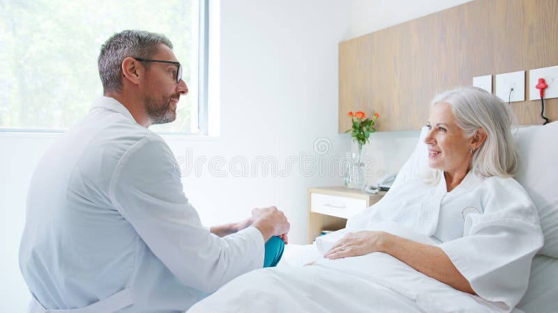 Medico maturo o chirurgo che parla con una paziente matura sdraiata nel letto dell'ospedale immagini stock libere da diritti