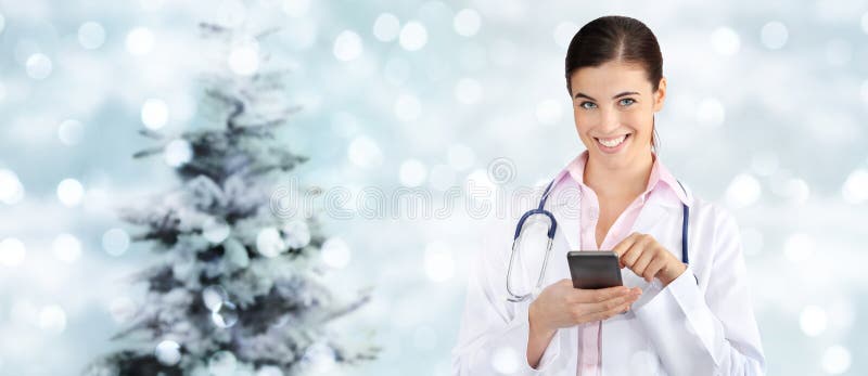 Medico sorridente di Natale con lo Smart Phone sulle luci vaghe fotografia stock libera da diritti Medico sorridente di Natale con lo Smart Phone sulle luci vaghe fotografia stock libera da diritti