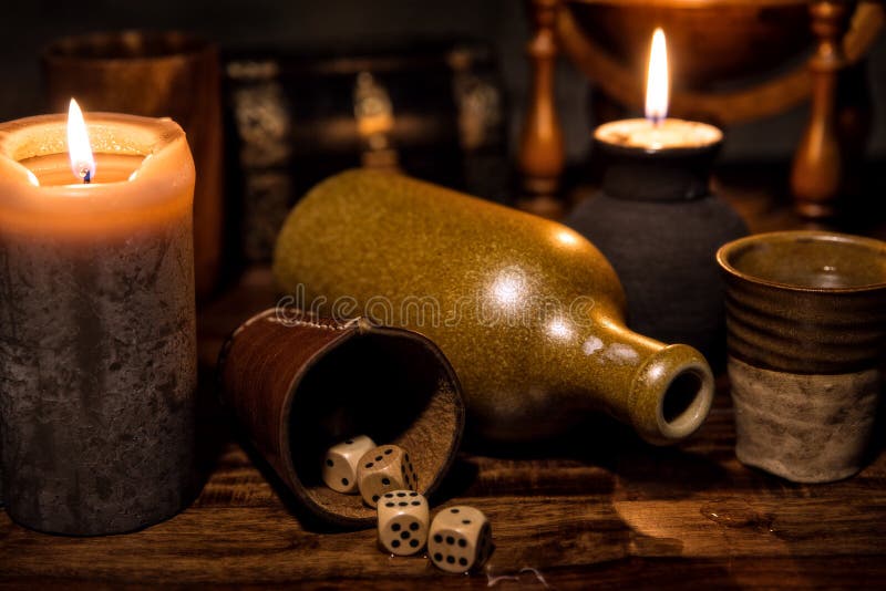 Medieval table with candles, a old bottle, a mug and wooden dice