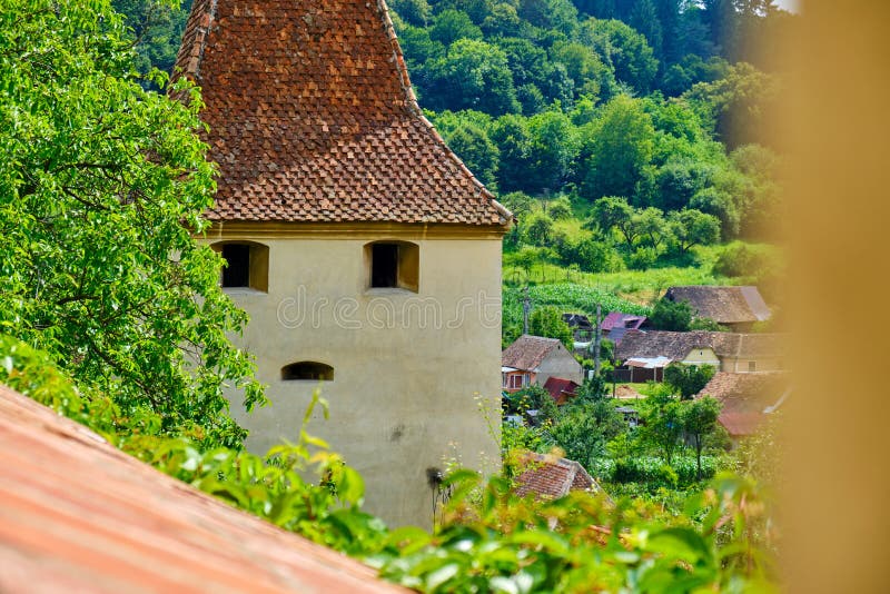 Medieval tower with windows shaped like eyes and mouth, in Biertan, Romania. Old building resembling a human face, partly hidden.
