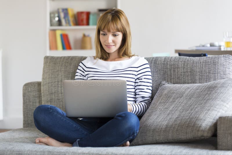 Medio volwassen vrouw op haar bank die laptop thuis met behulp van stock foto Medio volwassen vrouw op haar bank die laptop thuis met behulp van stock foto
