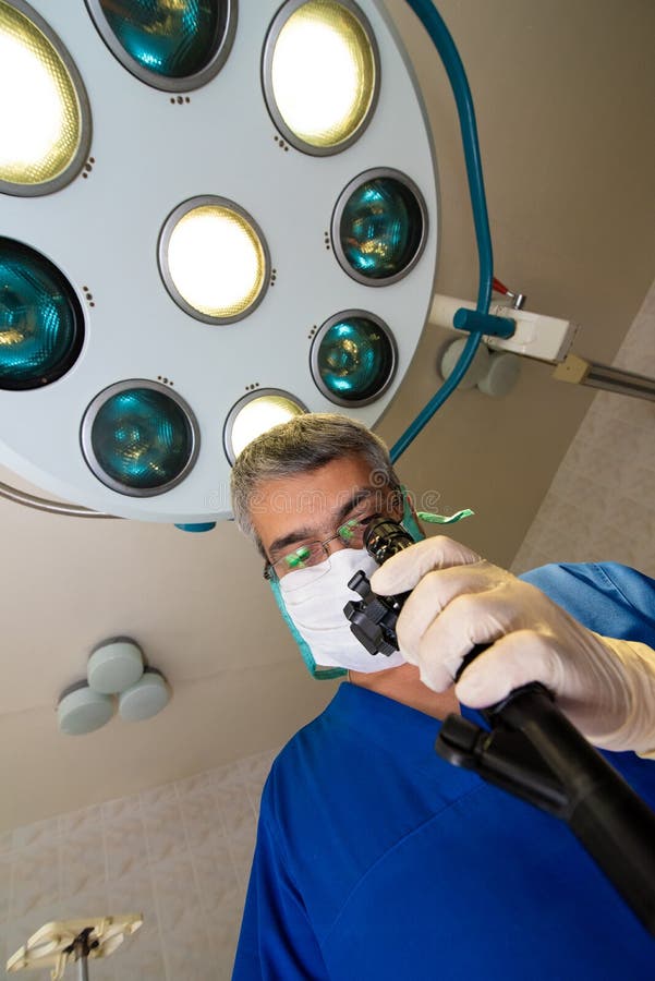 Medique em uma veste azul e em olhares da máscara no dispositivo foto de stock Medique em uma veste azul e em olhares da máscara no dispositivo foto de stock