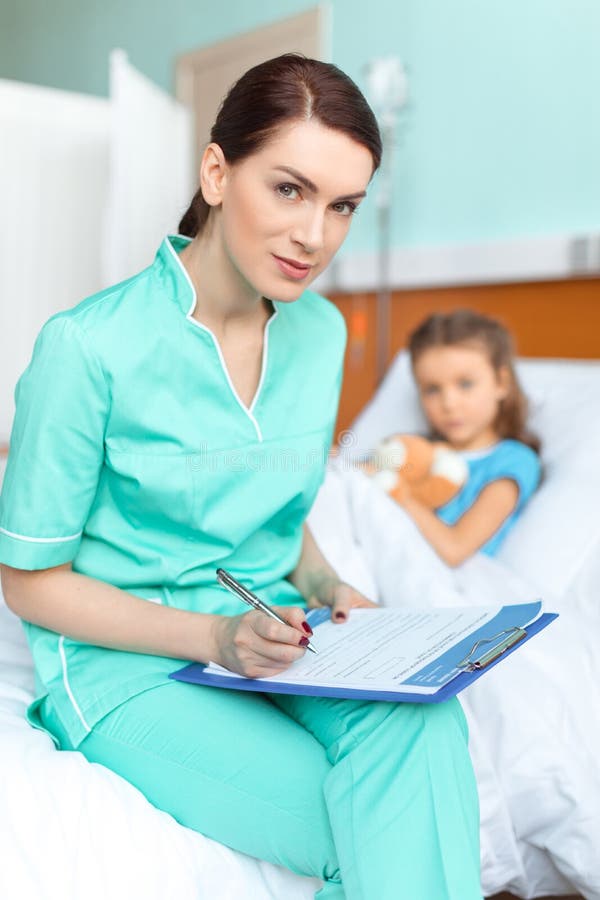 Medique a escrita no diagnóstico da prancheta da menina doente imagem de stock Medique a escrita no diagnóstico da prancheta da menina doente imagem de stock