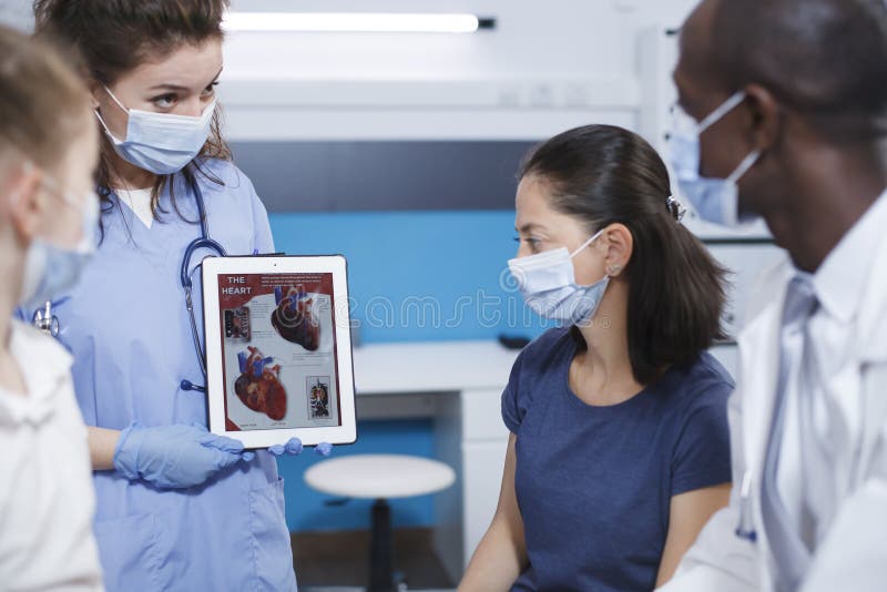 Detailed image of healthcare professionals using a tablet to explain to the female patients about the human heart. Nurse holds a device while the male doctor describes importance of medical checkups. Detailed image of healthcare professionals using a tablet to explain to the female patients about the human heart. Nurse holds a device while the male doctor describes importance of medical checkups.