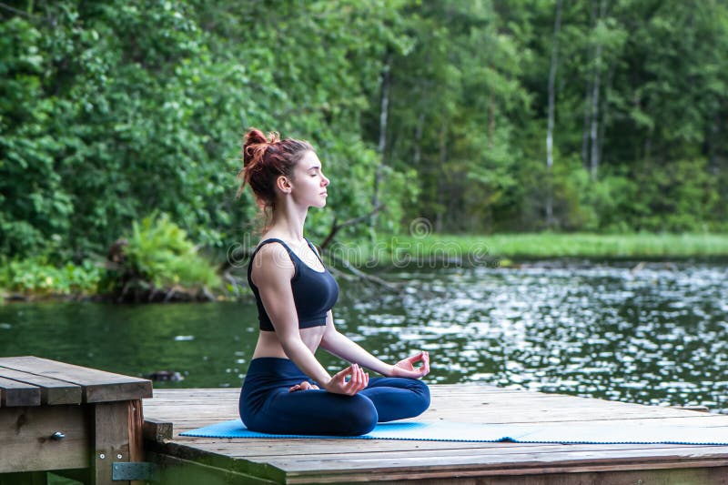 Meditación de la joven yogui en el muelle de un hermoso lago. El concepto de apaciguamiento, estilo de vida saludable fotos de archivo