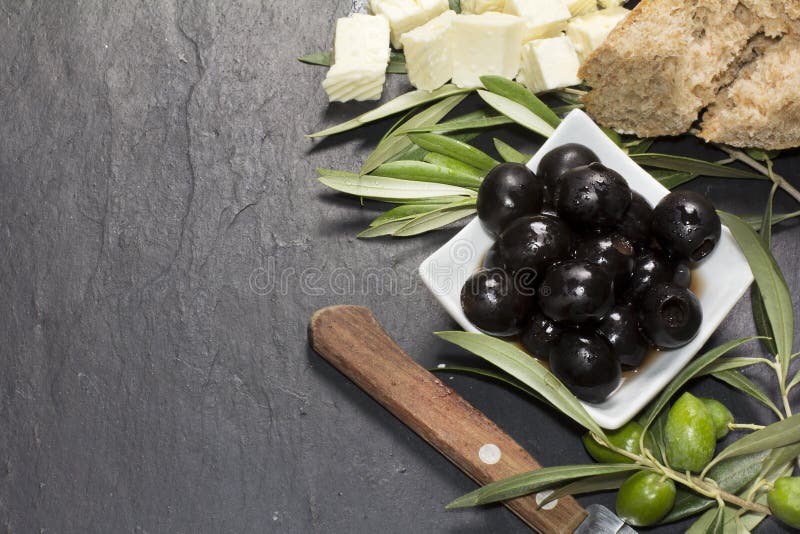 Mediterranean olives with feta cheese, virgin extra oil and fresh bread over dark stone royalty free stock image Mediterranean olives with feta cheese, virgin extra oil and fresh bread over dark stone royalty free stock image