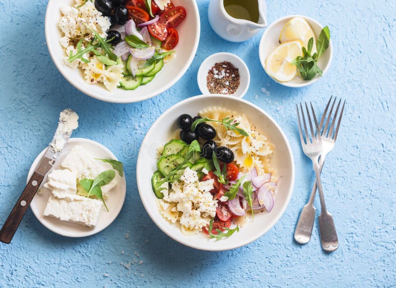 Mediterranean pasta salad. Pasta farfalle, tomatoes, cucumbers, olives, feta cheese and arugula salad. On a blue background, top