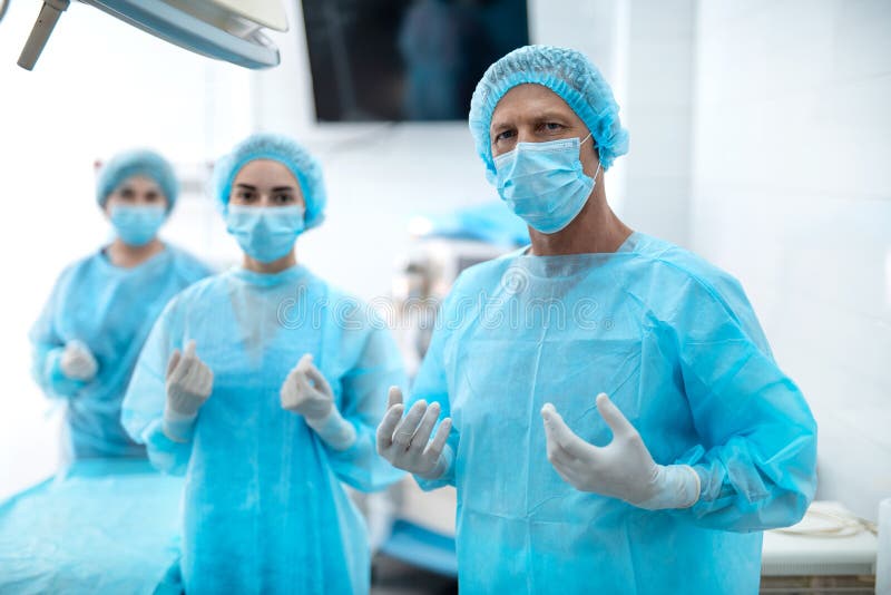 Medizinische Arbeitskräfte in den sterilen blauen Kleidern, die im Operationsraum aufwerfen lizenzfreie stockfotografie Medizinische Arbeitskräfte in den sterilen blauen Kleidern, die im Operationsraum aufwerfen lizenzfreie stockfotografie