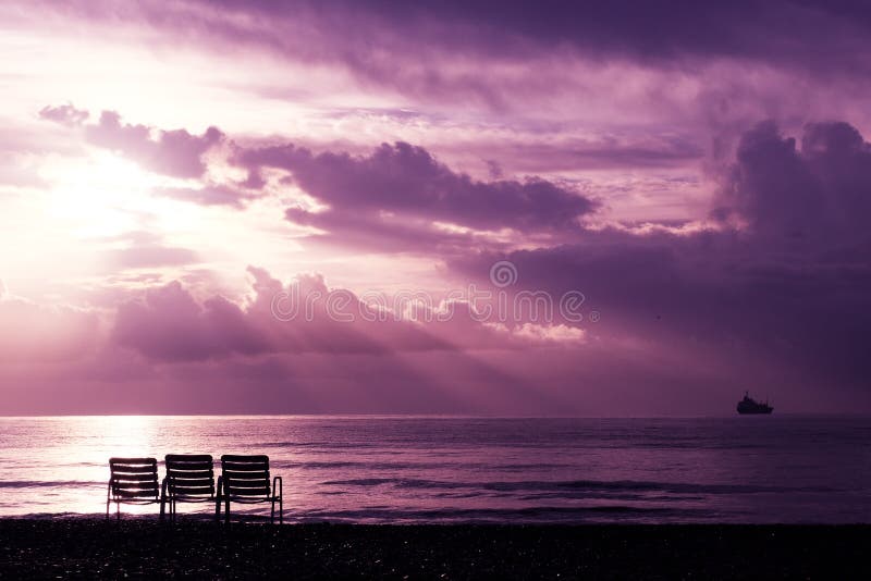Meerblick mit himmlischen hellen Strahlen und drei Stühlen auf dem Strand in Larnaka stockbild Meerblick mit himmlischen hellen Strahlen und drei Stühlen auf dem Strand in Larnaka stockbild
