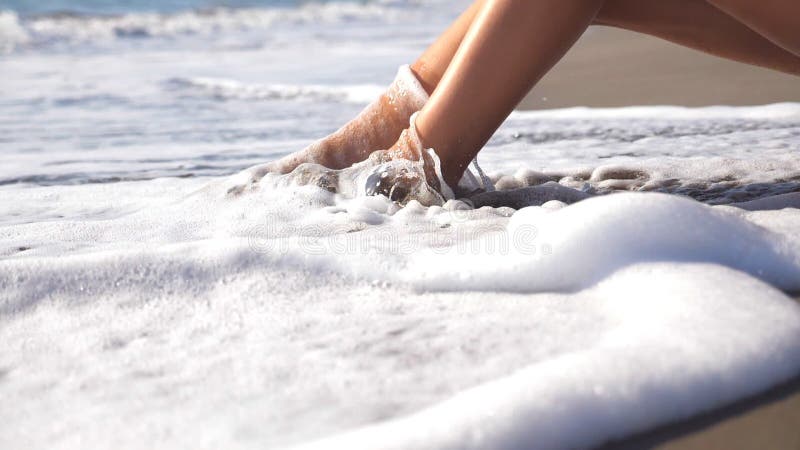 Meereswogen, die über gebräunten weiblichen Füßen sich waschen Beine des liegenden goldenen Sandes des sexy Mädchens auf Seestran