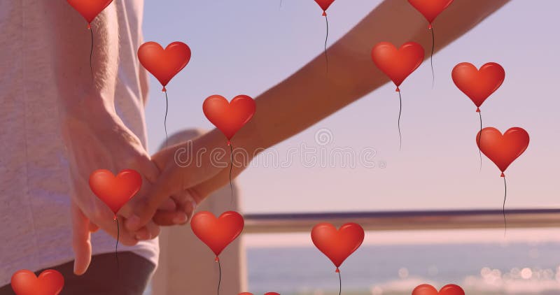 Meervoudige hartballonnen die tegen het middengedeelte van een paar zweven en die de handen op het strand houden
