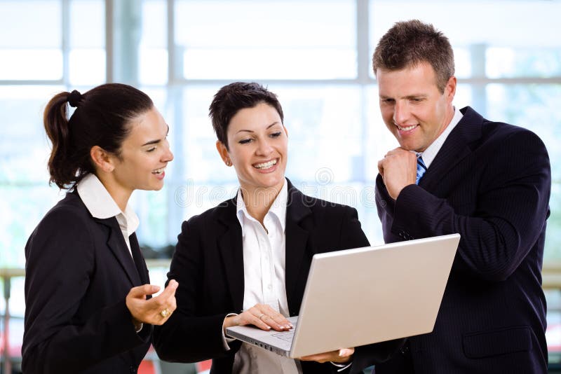 Three happy businesspeople standing and talking in office lobby, holding laptop computer in hand. Male hand holding businessman stock images, royalty-free photos and pictures