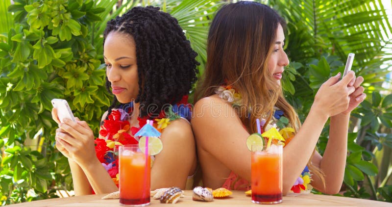 Meilleurs amis noirs et asiatiques des vacances utilisant des téléphones portables photo stock Meilleurs amis noirs et asiatiques des vacances utilisant des téléphones portables photo stock