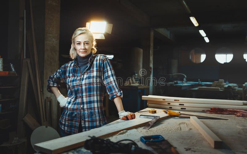 Meio bonito trabalhador de mulher envelhecido que levanta contra o fundo de uma oficina do woodworking Conceito de mulheres motiv