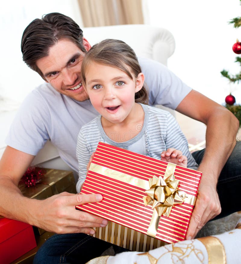 Surprised little girl opening a Christmas present with her father at home. Surprised little girl opening a Christmas present with her father at home