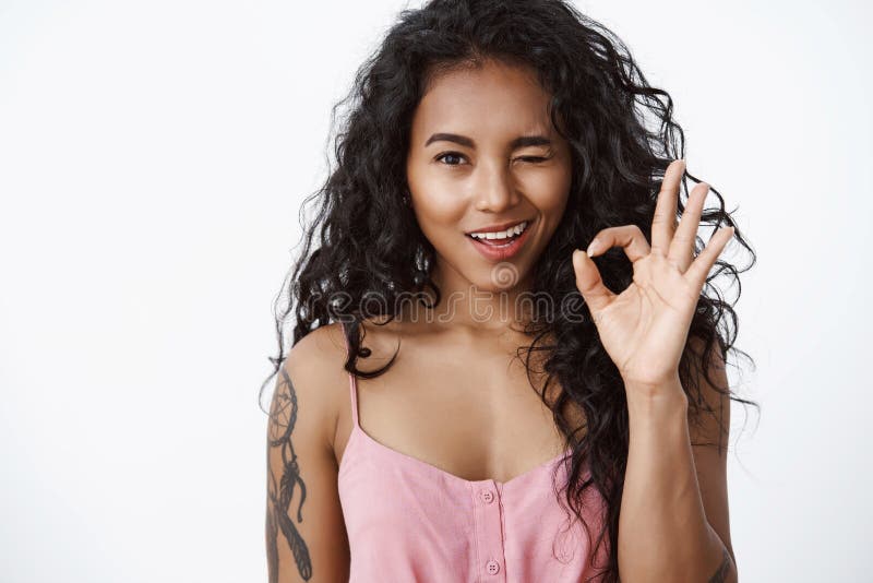Girl hinting everything under control. Attractive african-american curly-haired woman with tattoos, show okay, approval gesture, wink acceptingly, like excellent idea, white background. Girl hinting everything under control. Attractive african-american curly-haired woman with tattoos, show okay, approval gesture, wink acceptingly, like excellent idea, white background.