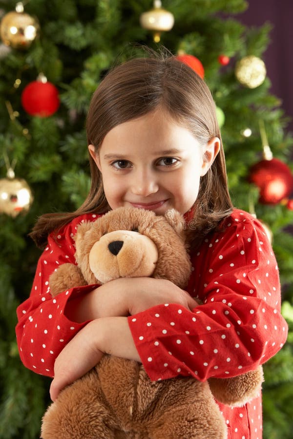 Meisje dat Teddy voor Kerstboom knuffelt