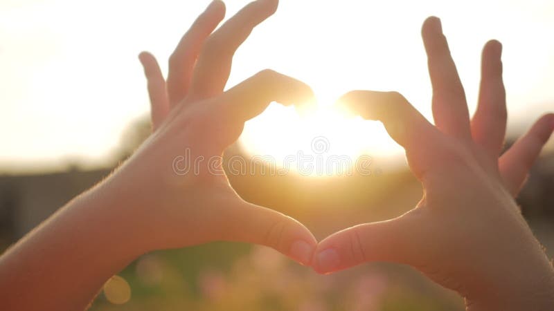 Meisje die harthanden tegen de hemel, kindhanden doen die een hartvorm met zonsondergangsilhouet vormen, liefde, droom, de zomer
