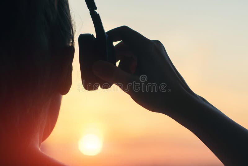 Meisje die in hoofdtelefoons aan muziek in de stad bij zonsondergang luisteren
