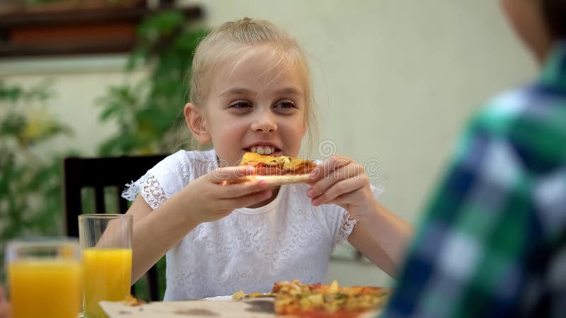 Meisje die pizza met broer die in koffie eten, verjaardag, favoriet voedsel vieren stock afbeelding Meisje die pizza met broer die in koffie eten, verjaardag, favoriet voedsel vieren stock afbeelding