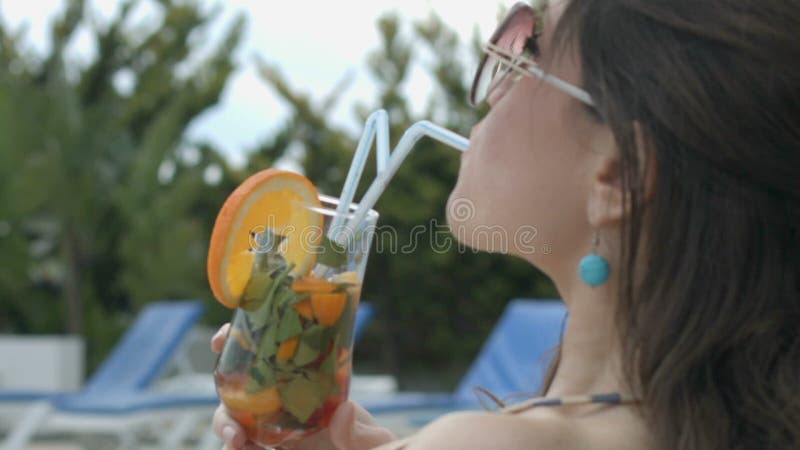 Meisje die van smaak van koele cocktailzitting genieten door pool van haar luxueus herenhuis