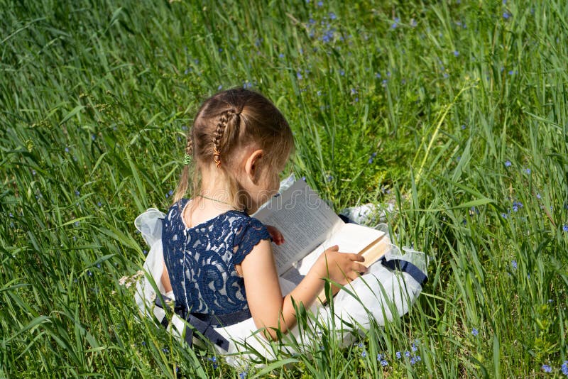 Meisje met een boek in de tuin Het jonge geitje readding een boek Een klein oud meisje 4-5 jaar zit op het gras en leest een boek stock afbeelding Meisje met een boek in de tuin Het jonge geitje readding een boek Een klein oud meisje 4-5 jaar zit op het gras en leest een boek stock afbeelding