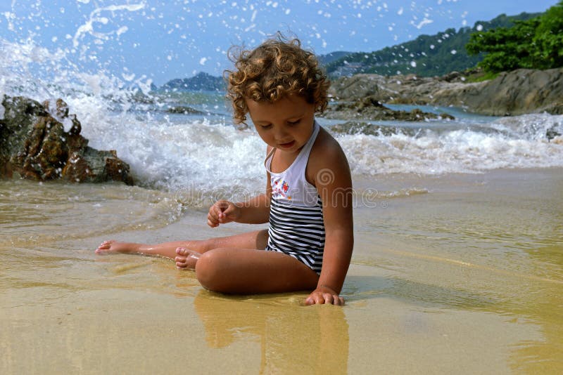 Meisje met krullen op het strand tegen de achtergrond van plonsen van de golf