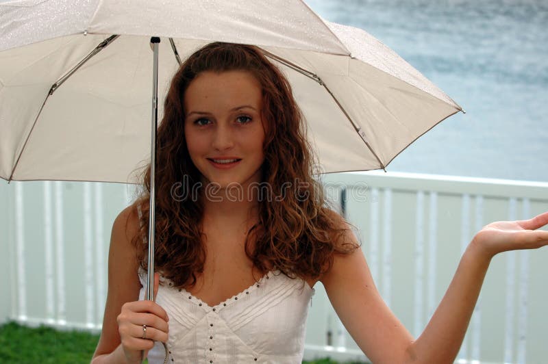 A pretty teen girl in the rain under an umbrella with the palm of her hand outside catching rain. A pretty teen girl in the rain under an umbrella with the palm of her hand outside catching rain