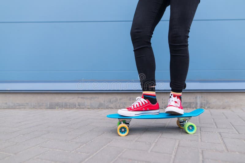 Meisje met rode kerels die op een blauw skateboard tegen een achtergrond van een blauwe muur berijden De kleding van kinderen stock foto Meisje met rode kerels die op een blauw skateboard tegen een achtergrond van een blauwe muur berijden De kleding van kinderen stock foto