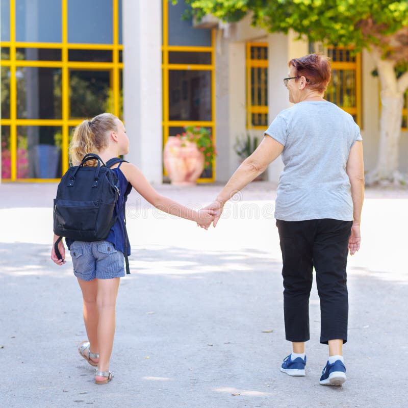 Meisje met schooltas of schooltas die aan school met grootmoeder lopen Achter mening stock fotografie Meisje met schooltas of schooltas die aan school met grootmoeder lopen Achter mening stock fotografie