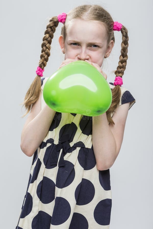 Meisje met Vlechten die in Polka Dot Dress Against White stellen Het blazen - omhoog Groene Hart Gevormde Luchtballon stock afbeelding Meisje met Vlechten die in Polka Dot Dress Against White stellen Het blazen - omhoog Groene Hart Gevormde Luchtballon stock afbeelding