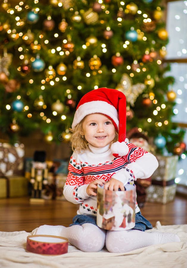 Meisje in rode santahoed het openen giften dichtbij een Kerstboom royalty-vrije stock fotografie Meisje in rode santahoed het openen giften dichtbij een Kerstboom royalty-vrije stock fotografie
