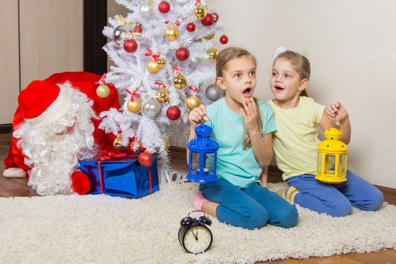 Meisjes met flitslichten van giften op Nieuwjarennacht de dromen, en gezette Santa Claus die stellen onder de Kerstboom voor royalty-vrije stock fotografie Meisjes met flitslichten van giften op Nieuwjarennacht de dromen, en gezette Santa Claus die stellen onder de Kerstboom voor royalty-vrije stock fotografie