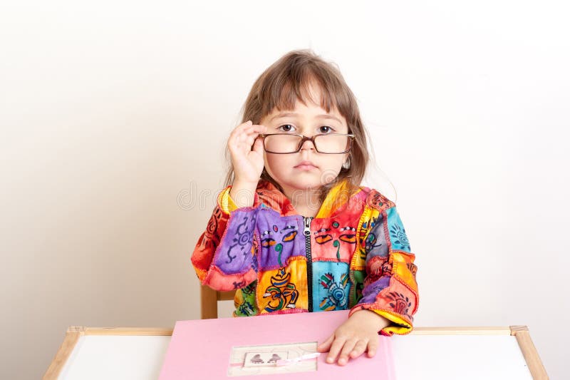 Meisjezitting bij het bureau en het kijken over haar glazen stock fotografie Meisjezitting bij het bureau en het kijken over haar glazen stock fotografie