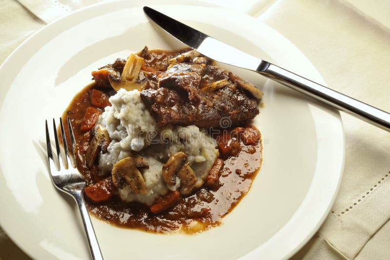 Beef cheeks in sauce with mushrooms and vegetables with mashed purple potatoes served on a white plate. Beef cheeks in sauce with mushrooms and vegetables with mashed purple potatoes served on a white plate.