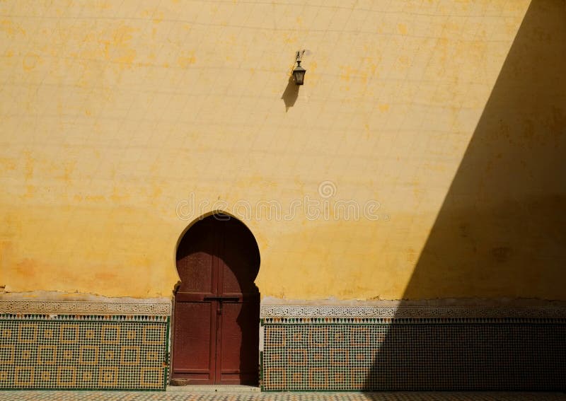 A vintage lamp on the yellow wall above moroccan red door and zellige tiles work.