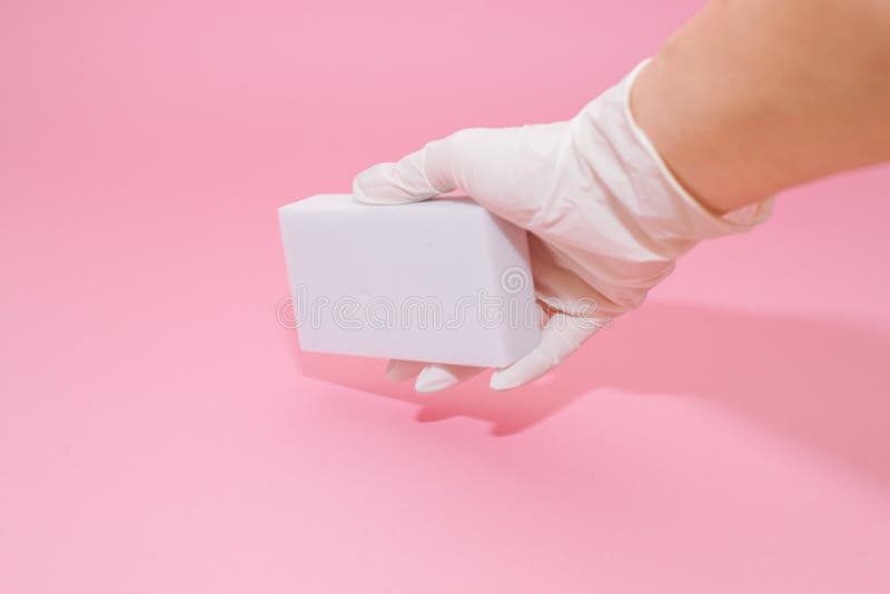 Human hand in white glove holds a white melamine household sponge for cleaning on pink background. Cleaning concept. Human hand in white glove holds a white melamine household sponge for cleaning on pink background. Cleaning concept