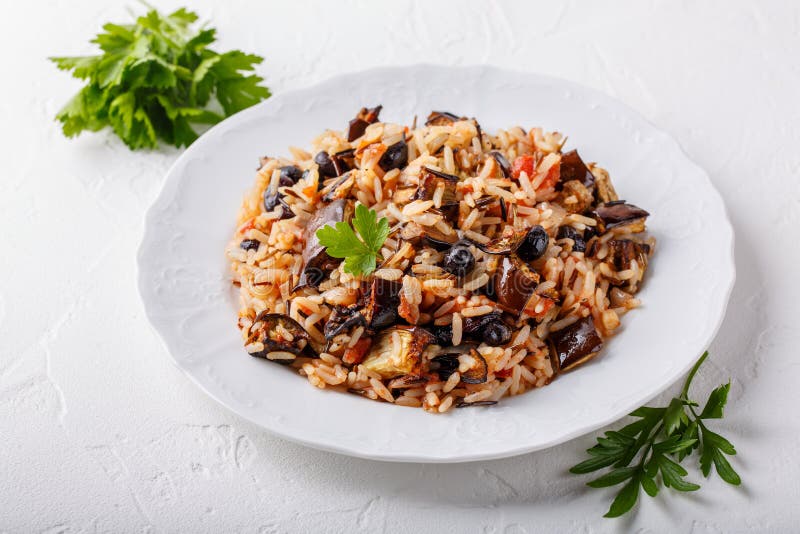 Melanzana pilaf servita in lamiera bianca. riso con melanzana uvetta nera e pomodori a tavola bianca. cibo vegetariano sano immagini stock libere da diritti