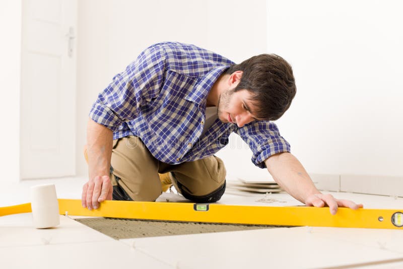 Home tile improvement - handyman with level laying down tile floor. Home tile improvement - handyman with level laying down tile floor
