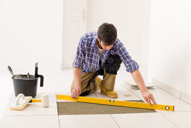 Home tile improvement - handyman with level laying down tile floor. Home tile improvement - handyman with level laying down tile floor