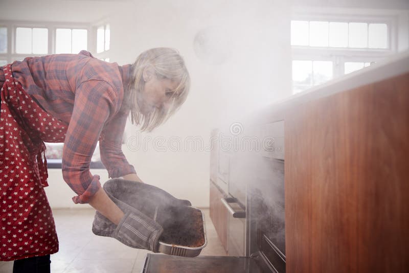Middle aged woman opening smoke filled oven in the kitchen. Middle aged woman opening smoke filled oven in the kitchen