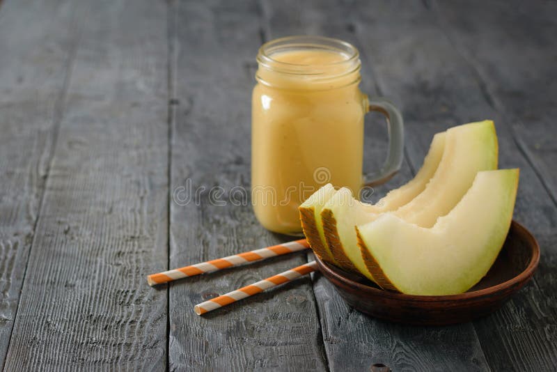 Melone, frullati della banana e dell'arancia e un melone appena fatti di tre fette su una tavola immagine stock
