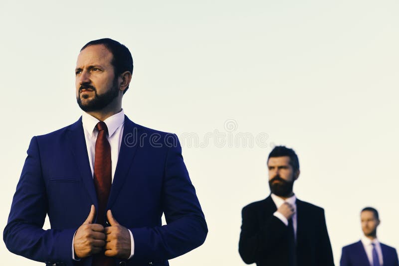 Men with beard and serious faces look aside. Businessmen touches jacket. Managers wear smart suits and ties. On blue sky background. Business and success royalty free stock photos Men with beard and serious faces look aside. Businessmen touches jacket. Managers wear smart suits and ties. On blue sky background. Business and success royalty free stock photos