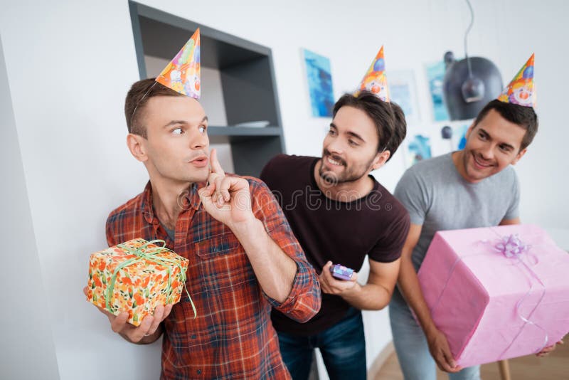 Men in birthday hats are preparing a surprise birthday party. They are preparing to meet the birthday girl. They are holding a presents in their hands.