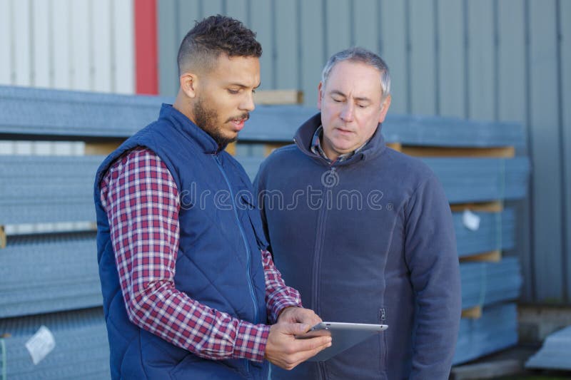 Men in builder\'s yard looking at tablet stock image
